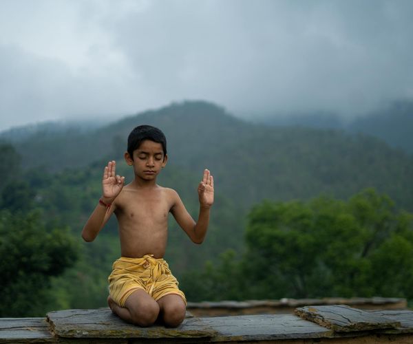 Person meditating outdoors with a beautiful natural landscape background.